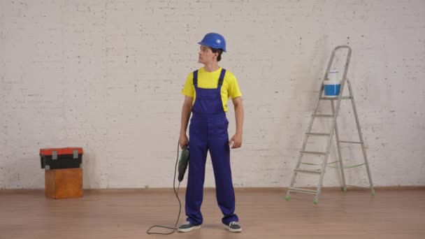 一个微笑的年轻工人站在正在翻新的房间里 举起钻头 在空气中穿孔 竖起大拇指的全长视频 公司广告 — 图库视频影像