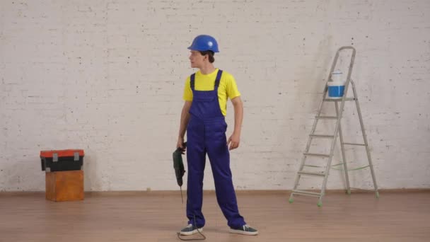 一个微笑的年轻工人站在翻新中的房间里 环顾四周 举起钻孔机 像把枪一样拿着 这段视频的全长视频 公司广告 — 图库视频影像