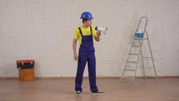 一个年轻的建筑工头站在正在翻新的房间里 通过防波堤 扩音器发出命令的全长录像 公司广告 — 图库视频影像