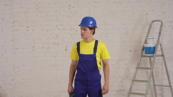 改装中の部屋に立っている若い建設作業員の中型ビデオ ドリルを上げ 空気中の森林破壊者と彼の筋肉を示しています メーカー 会社広告 — ストック動画