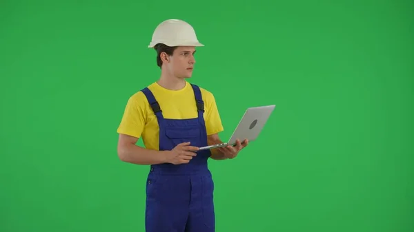 中型の緑色のスクリーンはラップトップを握り 周りを見回す若い建設労働者のクロマのキーショットを隔離しました 修理広告について アプリ サイト — ストック写真