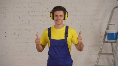 Tadilat altındaki odada kulaklık takan, kulaklık takan, ses kesen ve onay veren bir inşaat işçisinin orta boy fotoğrafı. Güvenlik önlemleri, koruma, şirket