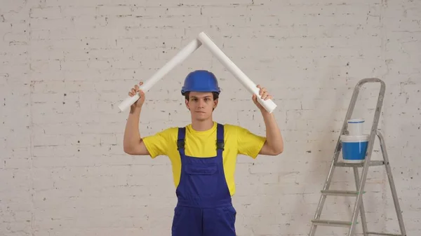 若い建設作業員の笑顔のビデオの中央ショットは 彼の頭の上に2つの巻き上げられた計画を立て 屋根を模倣しました メーカー 会社広告 安全性 信頼性 — ストック写真