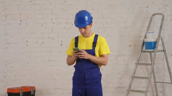 一个建筑工人站在房间里 手持智能手机 等待答案的中镜头 这个人看上去很温文尔雅 很关心别人 制造商 招聘公司广告 — 图库照片