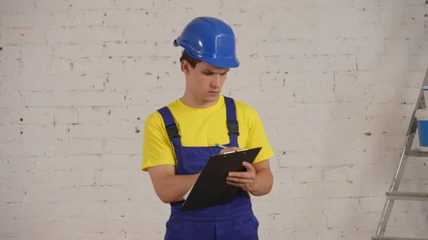 一名建筑工人站在房间内 拿着一块木板 文件夹 写下一些数据 区域研究的结果 制造商 — 图库照片