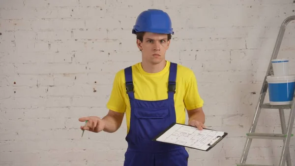 一个建筑工人站在房间内 手里拿着一块木板 文件夹和一支钢笔 耸了耸肩 不知道该写些什么 公司广告 — 图库照片