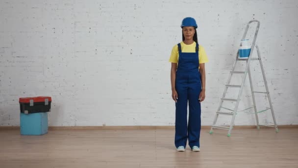 フレームの側面を指す部屋にユニフォームと硬い立場のダークスキンの若い女性建設労働者の全長ビデオ 広告のための場所 コンストラクション — ストック動画