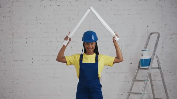 一个深色皮肤的年轻女建筑工人把头抬起两个卷起的计划 模仿一个屋顶的中等视频 制造商 公司广告 安全性 可靠性 — 图库视频影像