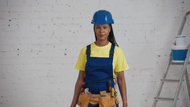 部屋に立っている暗い肌の若い女性建設作業員のミディアムビデオ ツールベルトを着て ツールボックスを持ち上げ 筋肉を見せます 会社広告 — ストック動画