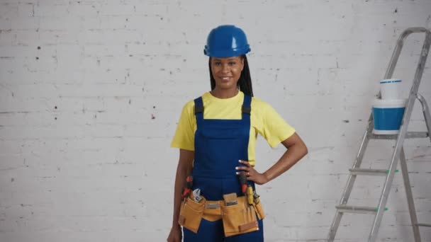 部屋に立っているダークスキンの若い女性建設労働者の中型ビデオは ツールベルトを着て 調整可能なレンチを示しています メーカー 会社広告 — ストック動画