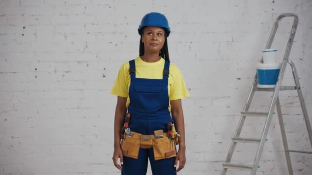 リノベーションの下に部屋に立っている制服を着た笑顔の若い女性建設作業員のミディアムビデオは 彼女の腰に彼女の手で抱きしめました メーカー — ストック動画