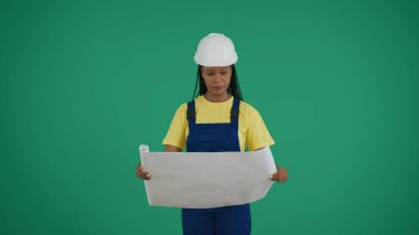 Koyu tenli genç bir inşaat işçisinin binanın planını incelerken çekilmiş orta yeşil ekran anahtar görüntüsü. İnşaat, tamir reklamı. Güvenilirlik.