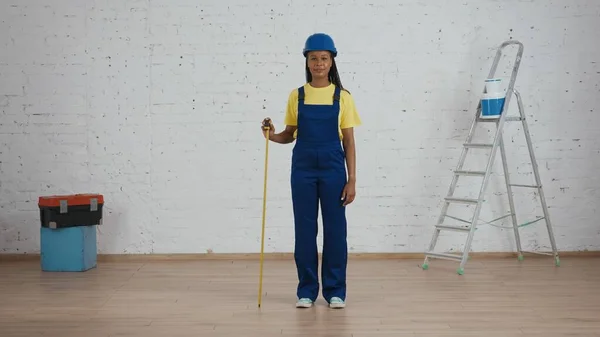 一个皮肤黝黑的年轻女建筑工头站在正在翻新的房间里 靠在建筑带子上 拍摄了全长照片 — 图库照片