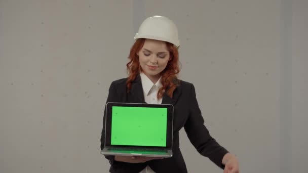 女性建築家が前に向かってラップトップスクリーンを保持し 緑色のスクリーンを指し 親指を上げます ハードハットでビジネス女性の肖像画と彼女の手のラップトップと灰色の背景 — ストック動画