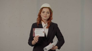 Bir kadın mimar elinde bir sertifika tutuyor, yüksek nitelikli olduğunu doğruluyor. İnşaat kaskı takmış bir iş kadınının portresi. Üzerinde taslak ve sertifikası var.