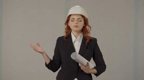 一个女建筑师冷静下来 闭上眼睛沉思 用手指做一个冥想的手势 一个戴着保护头盔 手里拿着设计图的女建筑师的画像 — 图库照片