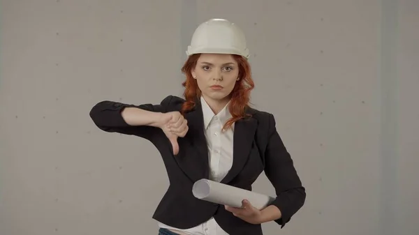 持怀疑态度 心烦意乱的女建筑师 表现出不喜欢的迹象 垂头丧气 一个头戴硬礼帽 手里拿着设计图的女人的画像 背景是灰色的 拒绝的概念 — 图库照片