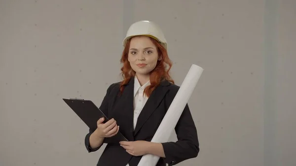 一个戴着保护头盔的女建筑师的画像 带有蓝图和灰色背景的工作室文件剪贴板 — 图库照片
