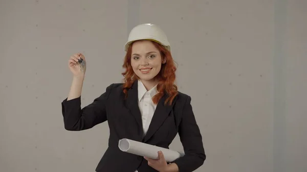 一个女建筑师拿着完工物件 公寓的钥匙 一个戴着保护头盔的女人的画像 在工作室里有灰色背景的蓝图 已完成项目 — 图库照片