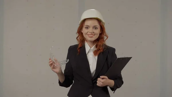 一个戴着防护头盔 戴着护目镜 带着剪贴板 背景灰暗的女建筑师的画像 — 图库照片