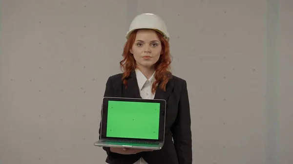 一位女建筑师正举着一个面向前方的笔记本电脑屏幕 工作室里 一个戴着硬礼帽 手里拿着笔记本电脑 背景灰暗的女商人的画像 广告区 工作空间 — 图库照片