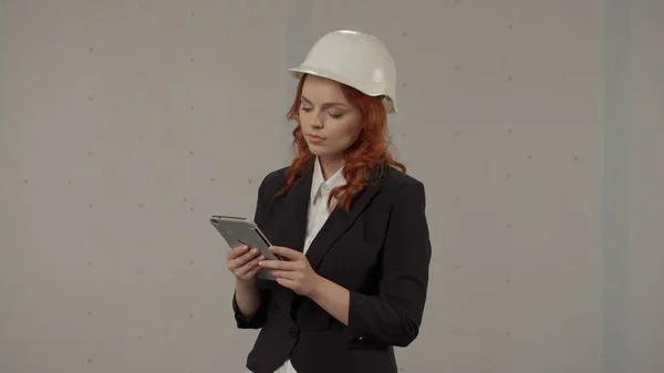 A woman architect takes notes in the tablet. Business woman in a protective helmet and with a tablet on a gray background in the studio