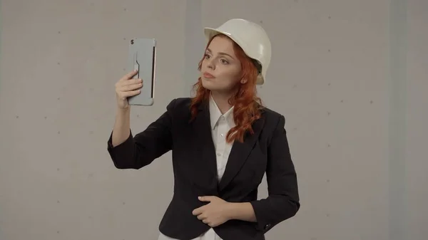 建筑师女人通过视频通话 用平板电脑自拍 戴着保护头盔穿着紧身衣的女商人们穿着灰色背景的工作服 — 图库照片