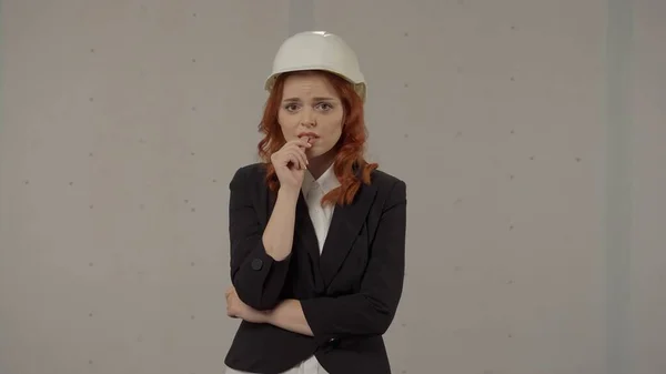 沮丧的女建筑师 咬手指 头戴防护头盔 身穿西装 头戴蓝色背景的红头发妇女 — 图库照片