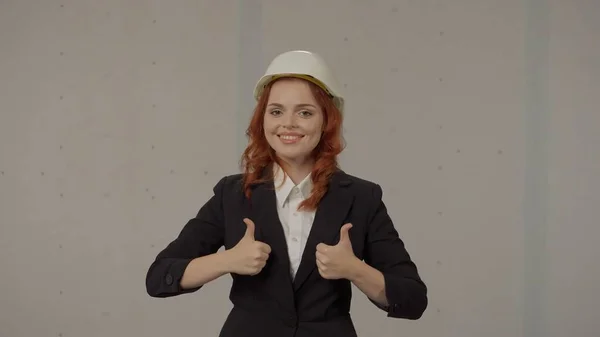 女建筑师竖起大拇指 身穿白色防护帽 头戴灰色背景工作室的女商人 — 图库照片