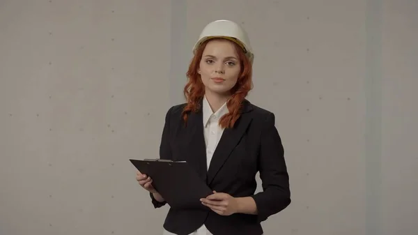 一个戴着保护头盔 带着灰色背景的剪贴板的女建筑师的画像 — 图库照片