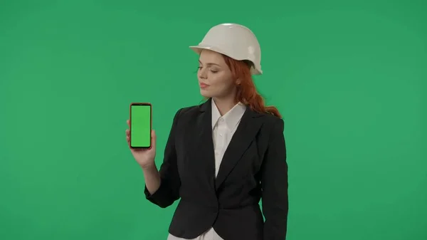女性アーキテクトはグリーンスクリーンスマートフォンを表示します スタジオのグリーンスクリーンの背景にあるヘルメットのビジネス女性の肖像画 広告エリア ワークスペース — ストック写真