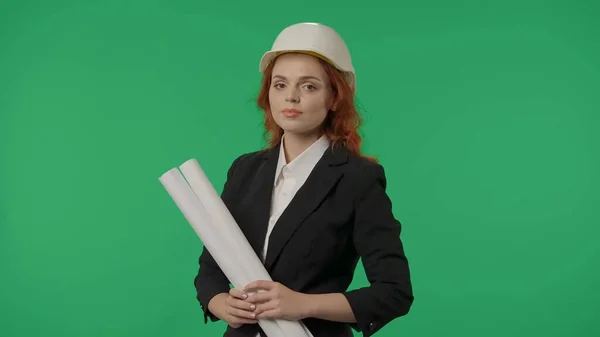 一个手里拿着设计图的年轻女建筑师的画像 女建筑师戴着防护头盔 穿着严格的西服 在工作室的绿屏背景下 建筑项目 — 图库照片