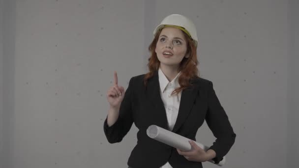 女性建築家は何かを指摘する グレーの背景にスタジオで彼女の手の青写真を持つヘルメットの女性の肖像画 Hdr Bt2020 Hlg材料を促進する — ストック動画