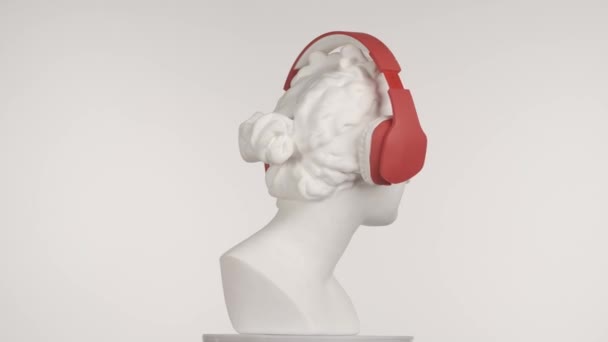 赤いヘッドフォンの美しい古代の女神金星大理石像のクローズアップショット プラットフォーム上で回転するロマン時代の女性バストの肖像画 白い背景に孤立した 創造的な抽象概念 Hdrについて — ストック動画