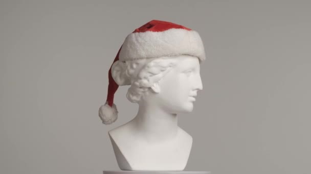 サンタの帽子で古代の女神ヴィーナス大理石像のクローズアップショット プラットフォーム上で回転するロマン時代の女性バストの肖像画 灰色の背景に孤立した 創造的な抽象概念 Hdr Bt2020 Hlgについて — ストック動画