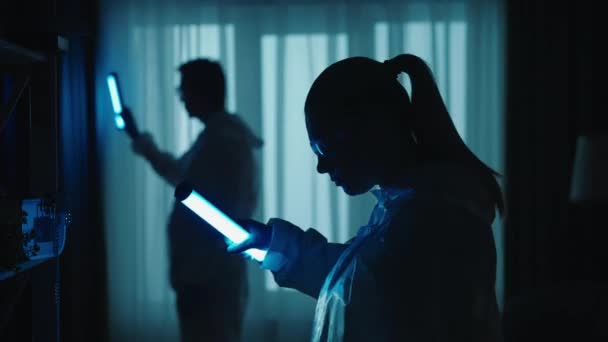 一队法医专家在犯罪现场工作 在一个黑暗的公寓里 蓝色的红色警笛照亮了房间 一个男人和一个女人在用紫外线灯寻找证据 — 图库视频影像