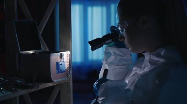 Fırça kullanan kadın bir kriminalist parmak izi için mücevher kutusunu inceliyor. Bir kadın, mavi polis sirenleriyle aydınlatılmış karanlık bir dairede fener kullanarak kanıt topluyor.