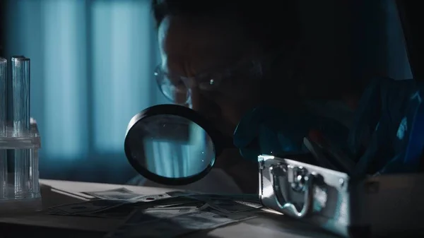 壮大なガラスを用いた法医学の専門家は 血液滴のドル紙幣を検査する 男は犯罪現場で検査を行い 青い光で照らされた暗いアパートで — ストック写真