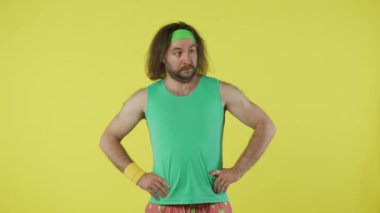 Spor kıyafetli bir adam spor salonuna geldi. Kafası karışmış ve şok olmuş görünüyordu. Yeşil kolsuz tişörtlü ve bantlı bir erkek portresi. Sağlık sigortası konsepti. Sarı arkaplanda izole edilmiş.
