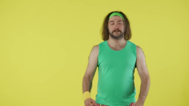 穿着运动服的人热身 嗅闻腋窝 在空旷的地方竖起大拇指做广告 绿色油箱顶部和帽带的男性画像 在黄色背景下隔离 — 图库视频影像