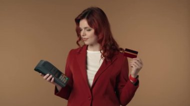 Bir elinde terminal, diğer elinde kredi kartı tutan neşeli, tatmin olmuş ve rahat bir genç kadının orta ölçekli videosu. Sonra kadın kameraya bakar. Ticaret ve bankacılık reklamı.