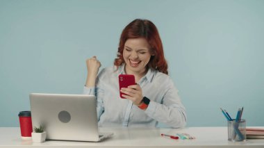 Olumlu bir haber aldıktan ya da bir şey öğrendikten sonra genç bir kadının telefonuna bakıp yumruğunu salladığı orta derece izole bir fotoğraf. Yaratıcı iş içeriği veya reklam.