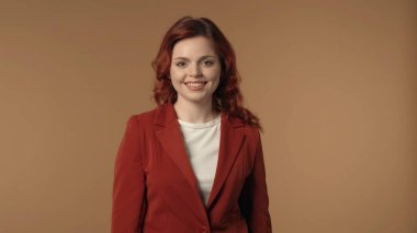 Genç ve başarılı bir iş kadınının, kahverengi arka planda dikilip doğrudan kameraya bakıp gülümserkenki görüntüsü. Kadın neşeli görünüyor. Yaratıcı iş içeriği.