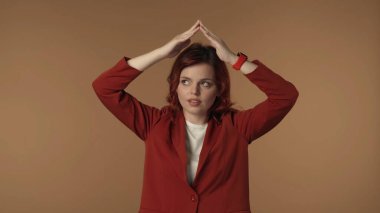 Tatmin olmamış, endişeli ve üzgün genç bir kadının el ele tutuşup çatıyı taklit ederken ve altından bakarken orta derece izole edilmiş görüntüsü. İş içeriği veya reklam.