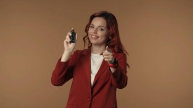 Şaşırmış, mutlu ve aktif genç bir kadının elinde araba anahtarı tutarken ve araba kazanabilecek ya da satın alabilecek izleyiciyi işaret ederken orta derecede izole edilmiş görüntüsü. Araba satıcısı, dağıtımcı, piyango reklamı.