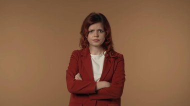 Sinirli ve tatminsiz genç bir kadının, kollarını kavuşturarak duygularını ifade etmek için vücut dilini kullanırken, gergin bir şekilde kameraya bakarken orta derecede izole edilmiş görüntüsü. Yaratıcı içerik veya reklam.