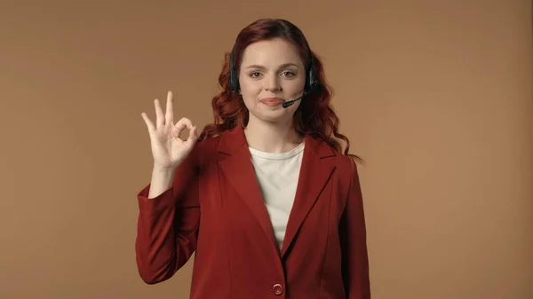 在呼叫中心的耳机中 一个快乐而轻松的年轻女性用右手展示了一个 的标志 商业广告和呼叫中心 — 图库照片