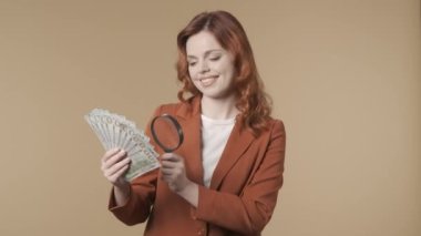 Genç bir kadının büyüteçle banknotlara bakıp gülümsediği orta ölçekli bir video. Para ve ticaretle bağlantılı yaratıcı içerik veya reklam. Maaş ve bankacılık. HDR BT2020 HLG