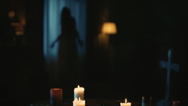 キャンドル クロス ビーズなどの魔法のツールでテーブルをキャプチャするビデオ 背景には ぼやけた女性のシルエットがあり 幽霊は窓の前で奇妙に動いています クリエイティブコンテンツ — ストック動画
