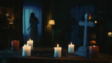 Üzerinde sihirli aletler olan bir masayı çekerken: mumlar, haçlar ve boncuklar. Arka planda bulanık bir kadın silueti var. Pencerenin önünde tuhaf bir şekilde hareket eden bir hayalet. Yaratıcı içerik.